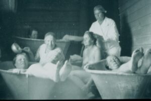 Vanhassa mustavalkovalokuvassa naisia pienissä kylpyammeissa